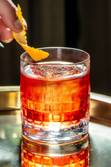 A classic cocktail served in a textured glass with a vibrant orange twist garnish, capturing a...