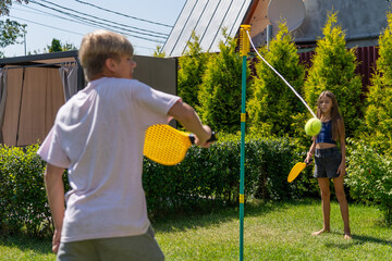 Youthful fun in the sun: A boy swings a racket at a tethered tennis ball as a girl awaits her turn...