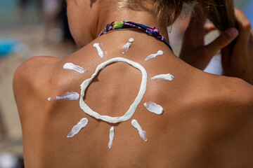 A playful sun design drawn with thick white sunscreen on a person's tanned back, symbolizing the...