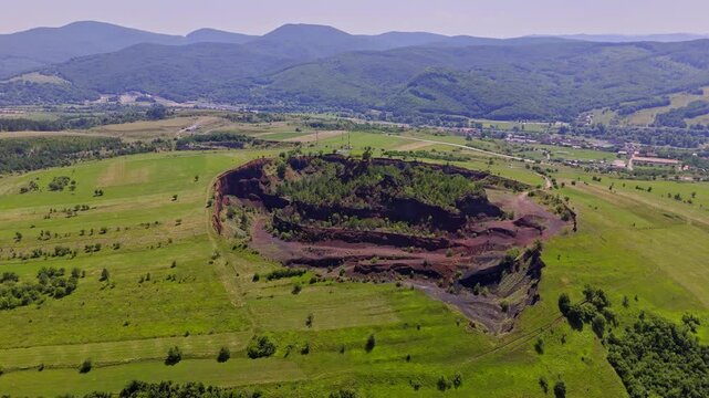 The extinct volcano from Racos, Romania. Aerial view of volcanic crater covered by green meadow and forest. View inside Volcano with lush vegetation in summer. Volcano ridge with vegetation. 