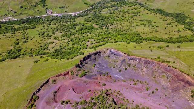 The extinct volcano from Racos, Romania. Aerial view of volcanic crater covered by green meadow and forest. View inside Volcano with lush vegetation in summer. Volcano ridge with vegetation. 