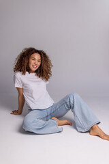 Curly Woman Sitting On Floor In White T-Shirt And Blue Jeans