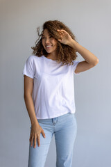 Beautiful Curly Woman Posing In White T-Shirt And Blue Jeans On Gray Background