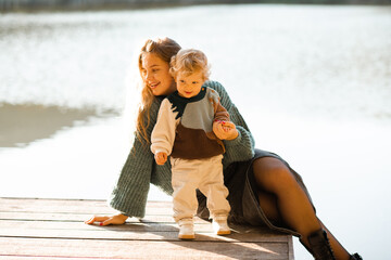 Smiling woman 24-29 year old with baby girl 1-2 year old wearing knitted sweaters over nature background. Autumn season. Motherhood.