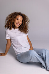 Curly Woman Sitting On Floor In White T-Shirt And Blue Jeans
