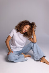 Curly Woman Sitting On Floor In White T-Shirt And Blue Jeans