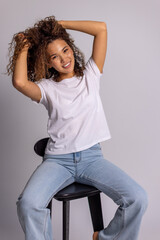 Curly Woman Sitting On Stool In White T-Shirt And Blue Jeans