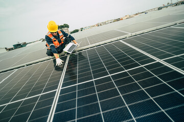 Solar panel technician inspects photovoltaic system on rooftop at midday while using a laptop for analysis