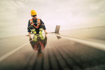 Worker in safety gear inspects solar panels on a cloudy day at a renewable energy facility