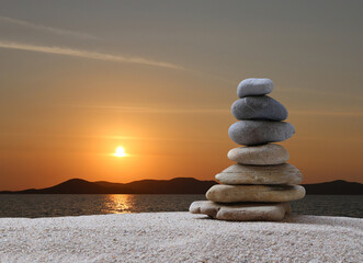 Stacked stones in a pyramid shape on a background of sea, mountains and sunset, copy space for design in your work, travel or zen theme.