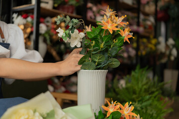 Asian female florist in apron smiling while designing a beautiful floral arrangement with her colleague in a flower shop. Concept of teamwork, creativity, floral business, and joyful workplace.