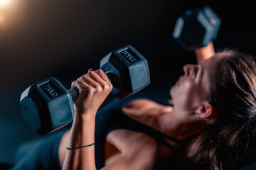 Dumbbell workout for chest involves a woman, training to enhance muscle strength in a dedicated gym space.