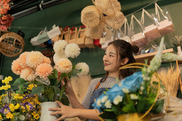 Asian female florist in apron smiling while designing a beautiful floral arrangement with her...