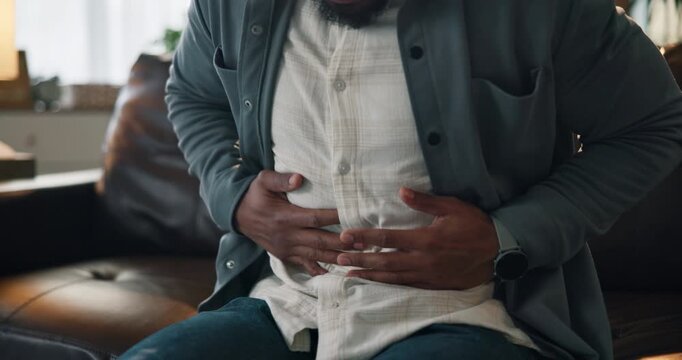 Hands, stomach pain and man on sofa, sick or tummy bug with cramp, indigestion or food poisoning. Person, abdomen and illness with inflammation, constipation and belly ache on couch at apartment