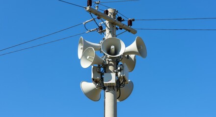 Utility pole with multiple horn speakers against blue sky.