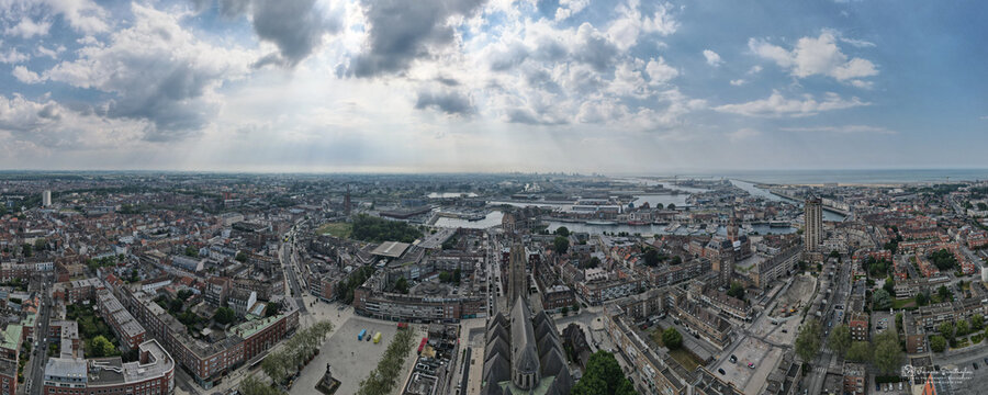 Aerial view of sun rays piercing through dramatic clouds, illuminating the city and harbor, revealing textures of buildings and waterways, Dunkirk, France.