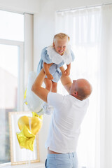 Father joyfully lifts daughter during cheerful celebration in bright indoor space