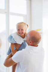 Father joyfully lifts daughter in bright indoor setting during a cheerful moment