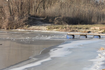 Wooden зpier on the shore of a frozen river in early spring