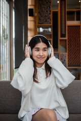 A young woman wearing headphones, sitting on a sofa, enjoying music in a stylish and cozy living room.