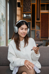 A young woman enjoys music with headphones while using her smartphone in a stylish cafe environment.