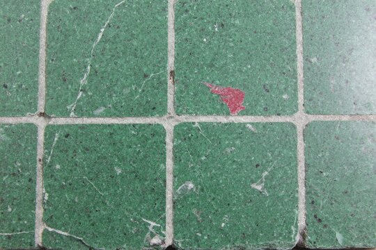 Green mosaic tile surface with cracks and red mark