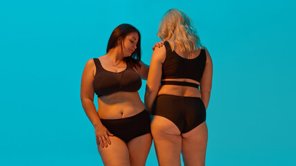 Two women in black underwear posing confidently against blue background. Concept of body...