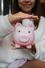 Close-up of a woman holding a pink piggy bank, symbolizing savings and financial security in a cozy home environment.