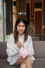 Smiling woman in casual attire deposits a coin into a pink piggy bank, symbolizing savings and financial planning.