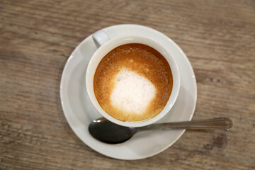 A cup of cappuccino on a saucer with a spoon on a wooden table