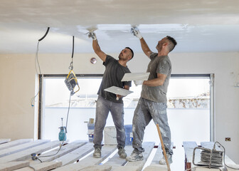 Two men working standing on scaffoldings, use trowel and hawk to plaster ceiling, construction