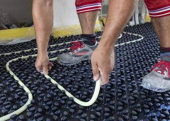 Man installing plastic pipes on insulation boards for underfloor heating system. House construction