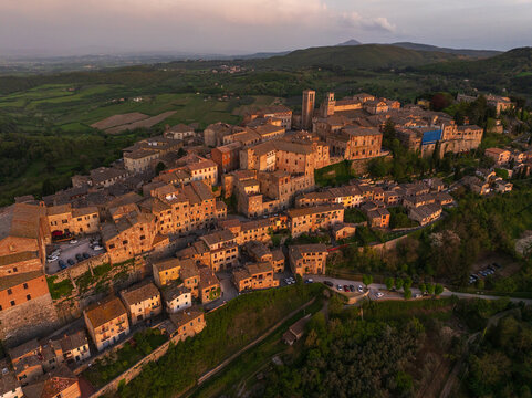 Fototapeta Aerial view of ancient terracotta rooftops cascading down the hillside towards lush greenery, crowned by the medieval towers of Montepulciano, Tuscany, Italy.