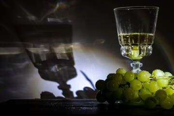 Racimo de uvas verdes en una copa de vino blanco alumbradas por un foco marcando las sombras de...