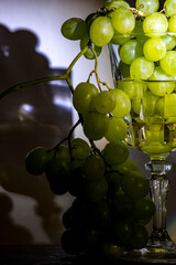 Racimo de uvas verdes en una copa de vino blanco alumbradas por un foco marcando las sombras de...