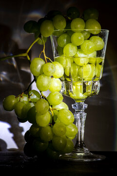 Racimo de uvas verdes en una copa de vino blanco alumbradas por un foco marcando las sombras de tras 