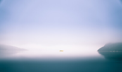 Kayaker paddling through misty Norwegian fjord surrounded by cliffs calm reflective water creates...