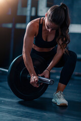 Barbell prep with added weights engages a woman, preparing for training to boost strength and fitness in a dedicated gym space.