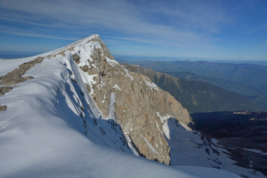 Aerial view of the rugged, snow-capped peak piercing the azure sky, a stark contrast to the lush green slopes below, Litochoro, Larisa, Greece.