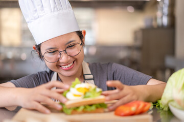 Smiling Young Asian Female Chef Preparing Sandwich in Kitchen