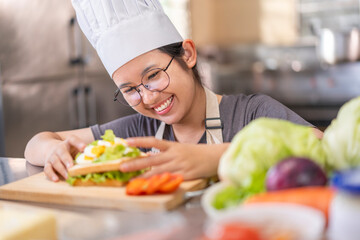 Smiling Young Asian Female Chef Preparing Sandwich in Kitchen