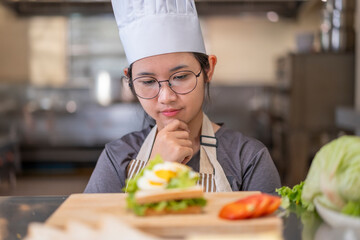 Thoughtful Young Asian Female Chef Evaluating Sandwich in Commercial Kitchen