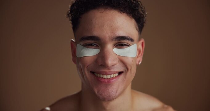 Face, eye patches and man with dermatology, smile and skincare on brown studio background. Portrait, space and happy person with cosmetics, spa wellness and grooming with healthy skin and laughing