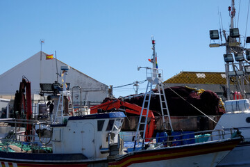 Fishing boats docked in harbor on sunny day with clouds