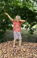 boy dances with joy standing on pile of freshly dug potatoes of different shapes and sizes, pleased...