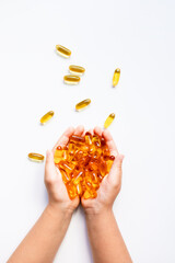 Child hands holding yellow fish oil capsules against white background