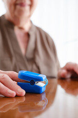 Vertical close-up of senior woman using pulse oximeter at home, with copy space.