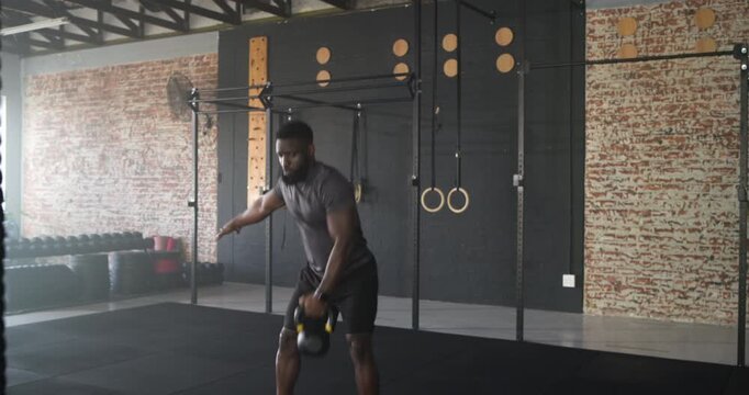 African American man swinging and pressing yellow kettlebell overhead at gym building strength