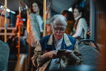 Senior man using smartphone while traveling by bus at night