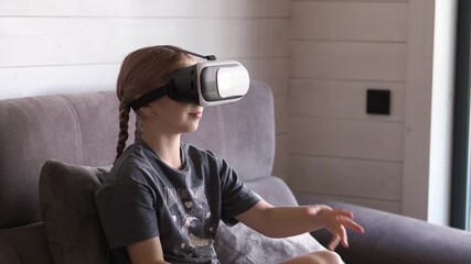 A girl wearing 3D virtual reality glasses studies an online simulation of the virtual world. A small, serious child gets experience in education with the help of virtual reality glasses. - Powered by Adobe